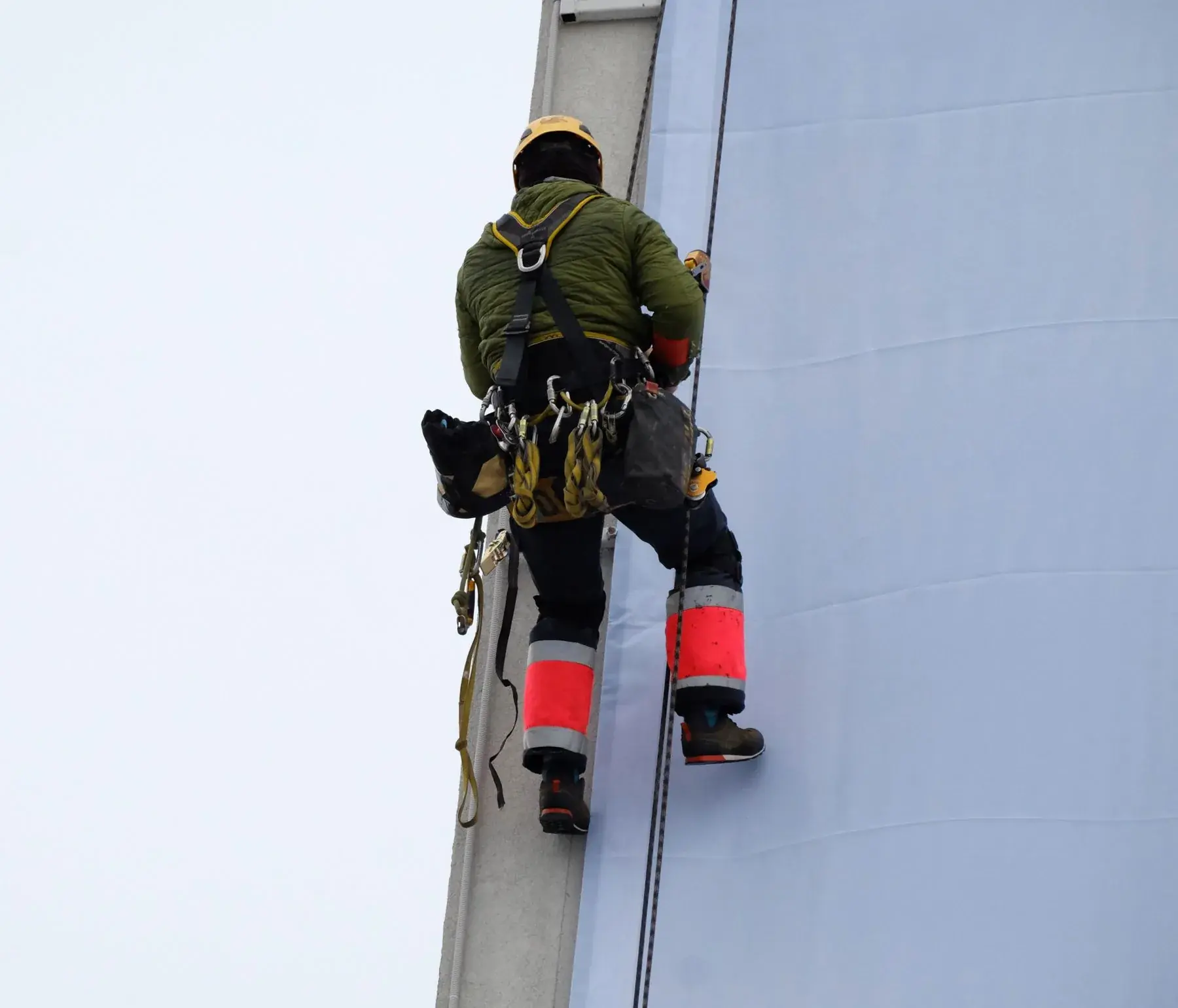 Técnico de acesso por corda realizando manutenção em fachada de edifício